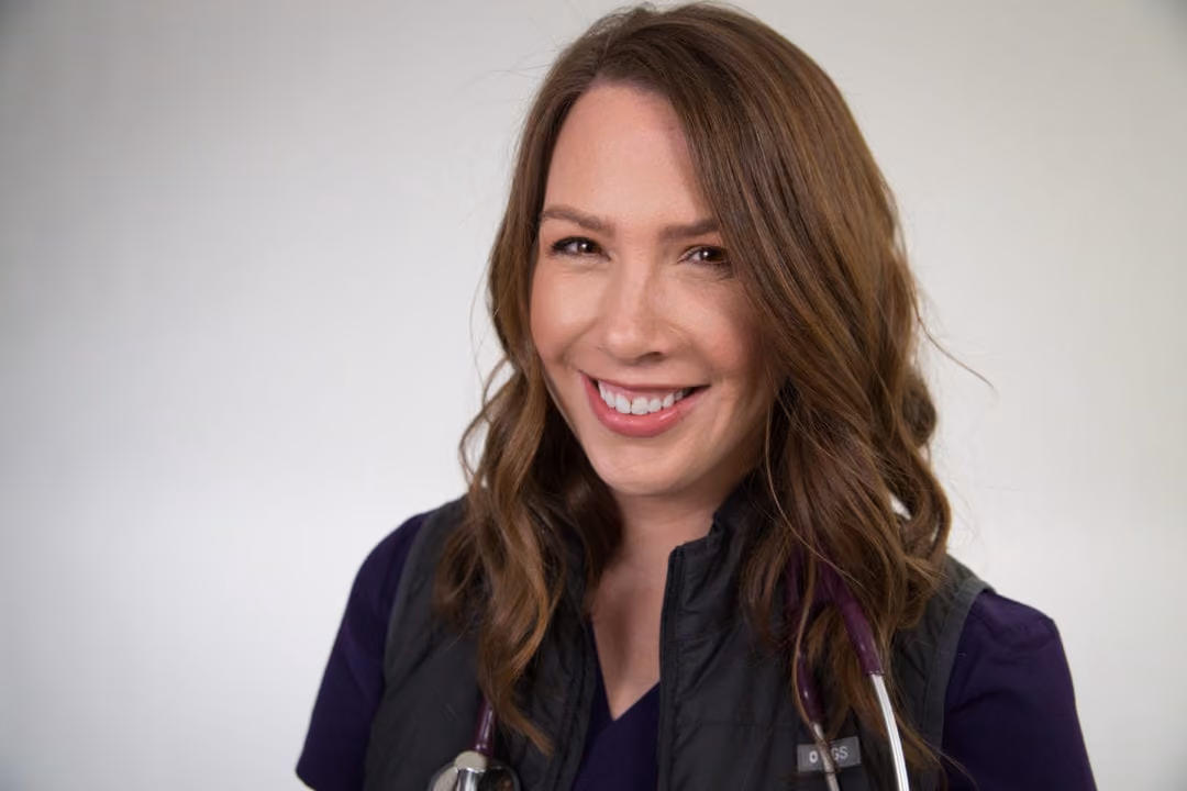Smiling woman with brown hair wearing purple scrubs and a stethoscope around her neck.