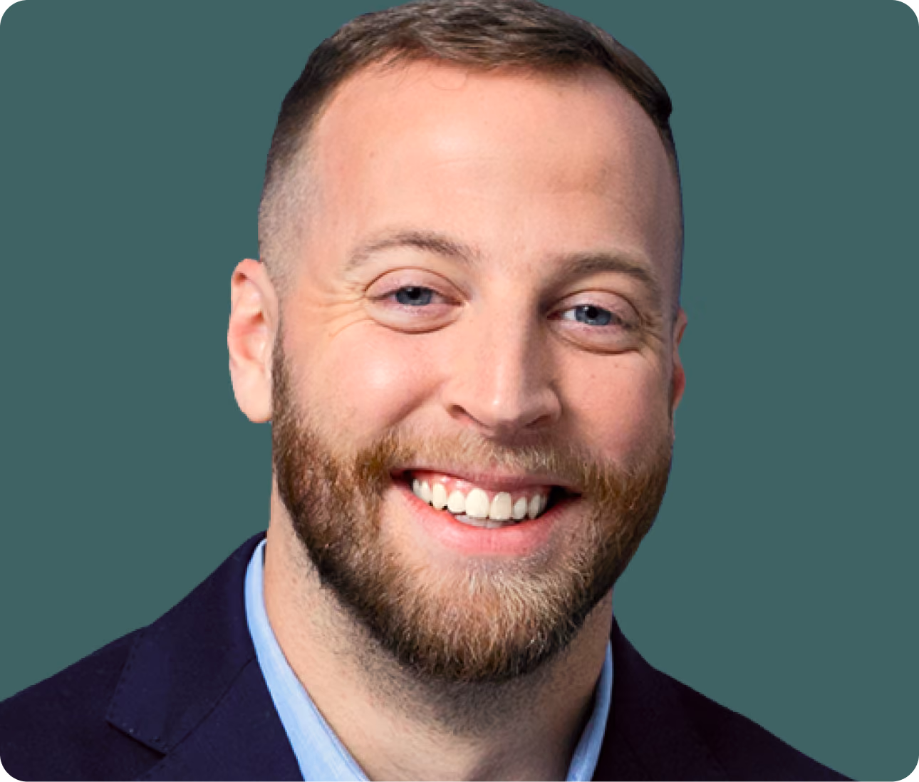 Smiling man with short brown hair, beard, and blue eyes wearing a navy blazer and light blue shirt.