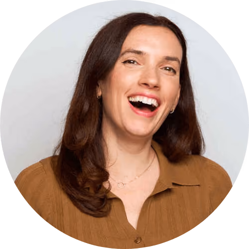 Woman with long brown hair laughing, wearing a brown shirt and delicate necklace.