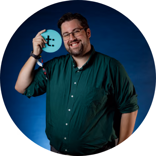 Smiling man with glasses in green shirt holds a blue circle with a black logo on a blue background.