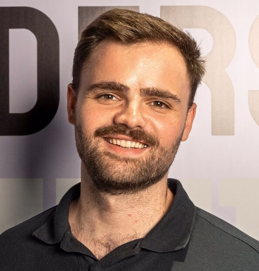 Smiling man with short brown hair and beard wearing a black collared shirt.