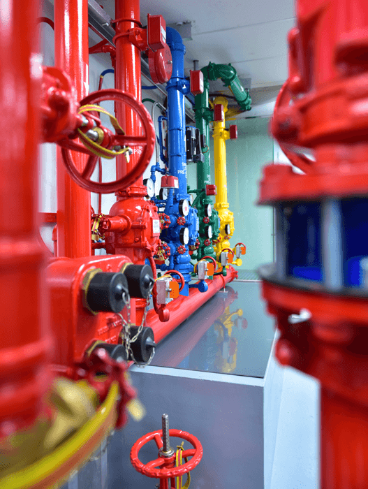 Color-coded industrial pipes and valves in red, blue, green, and yellow inside a utility room.