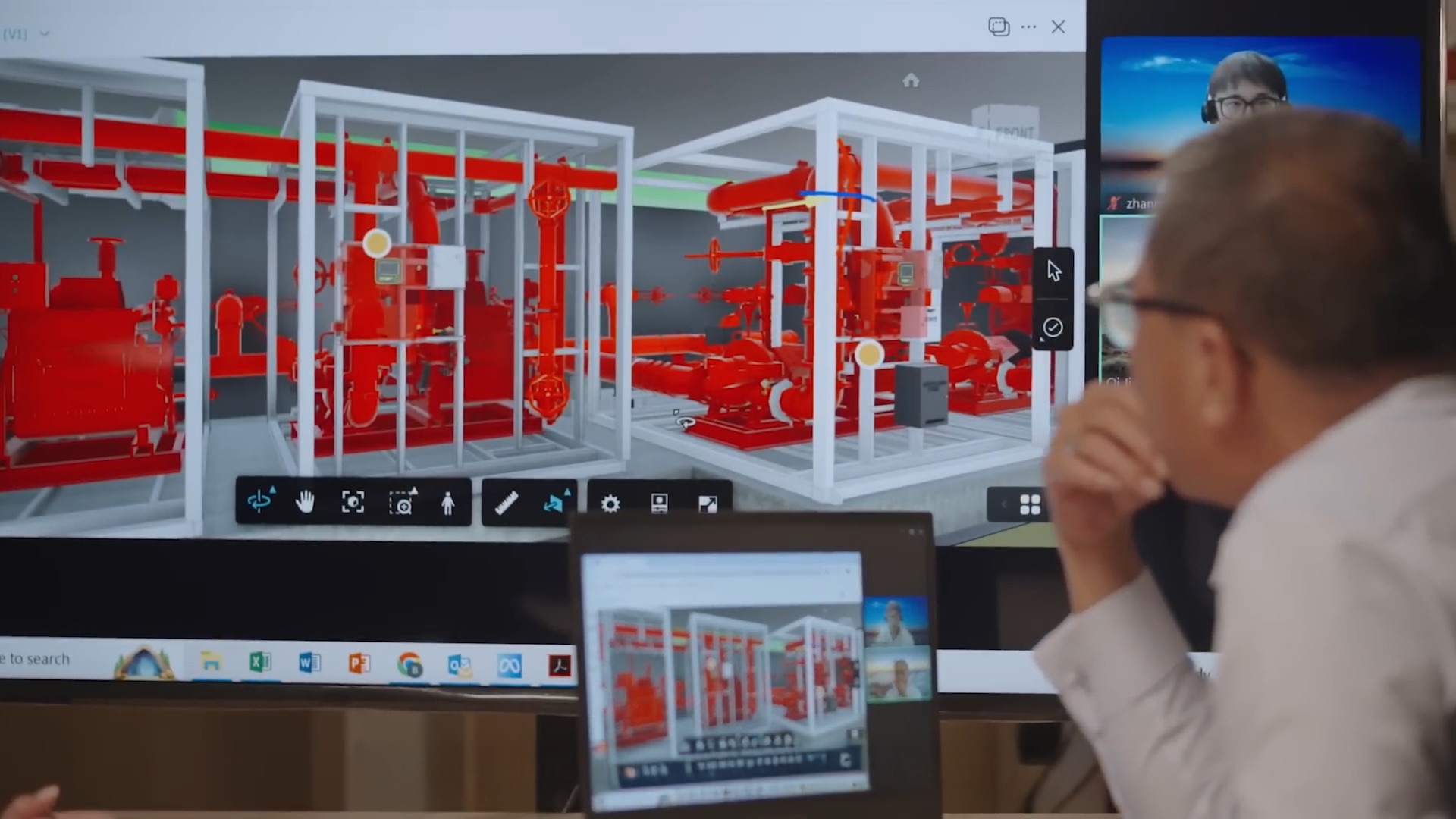 Person observing a computer screen and large monitor displaying a detailed 3D model of industrial red piping systems in white framing.