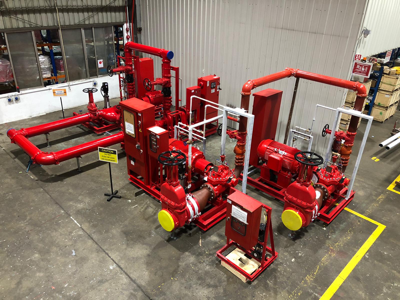 Industrial red fire pump system with large valves and pipes inside a warehouse.