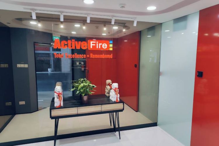 Modern office entrance with glass walls displaying 'Active Fire Total Excellence - Remembered' and a table holding a potted plant and decorative lion statues.
