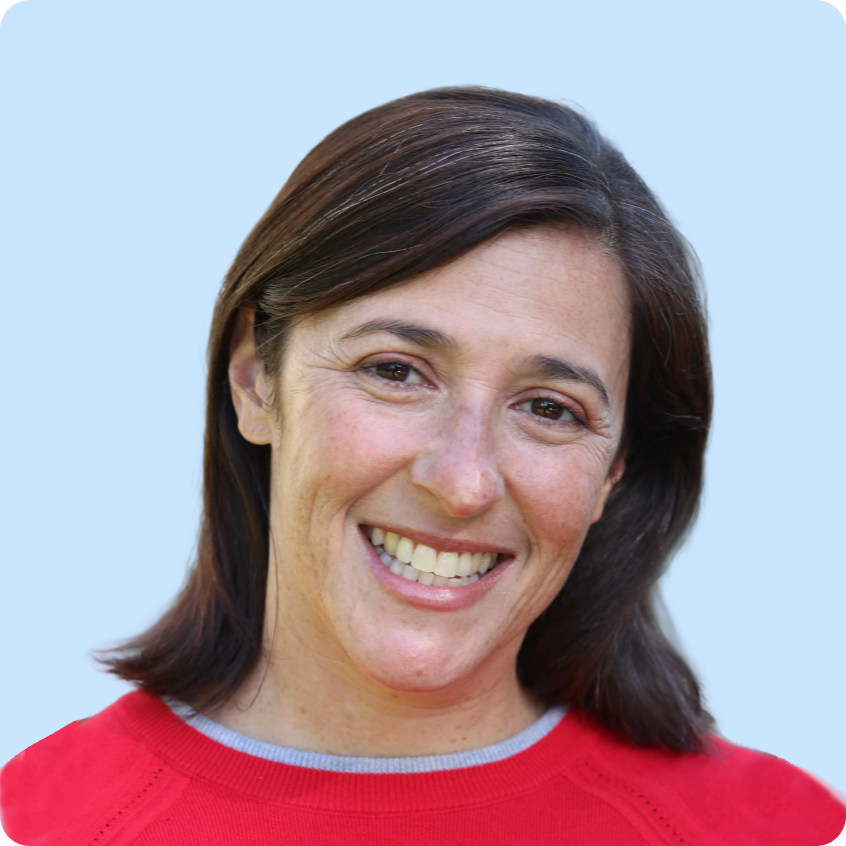 Smiling woman with dark brown hair wearing a red sweater against a light purple background.