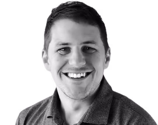 A man with a blue shirt and a beard smiling for the camera.