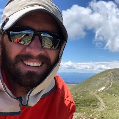 A man wearing a red shirt and a hat smiles for the camera.