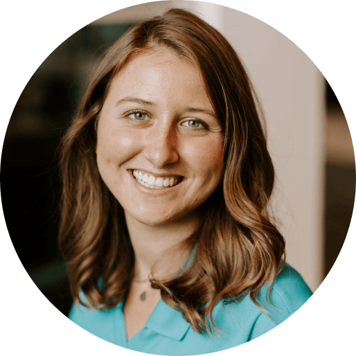 A woman with a blue shirt and a necklace smiling at the camera.