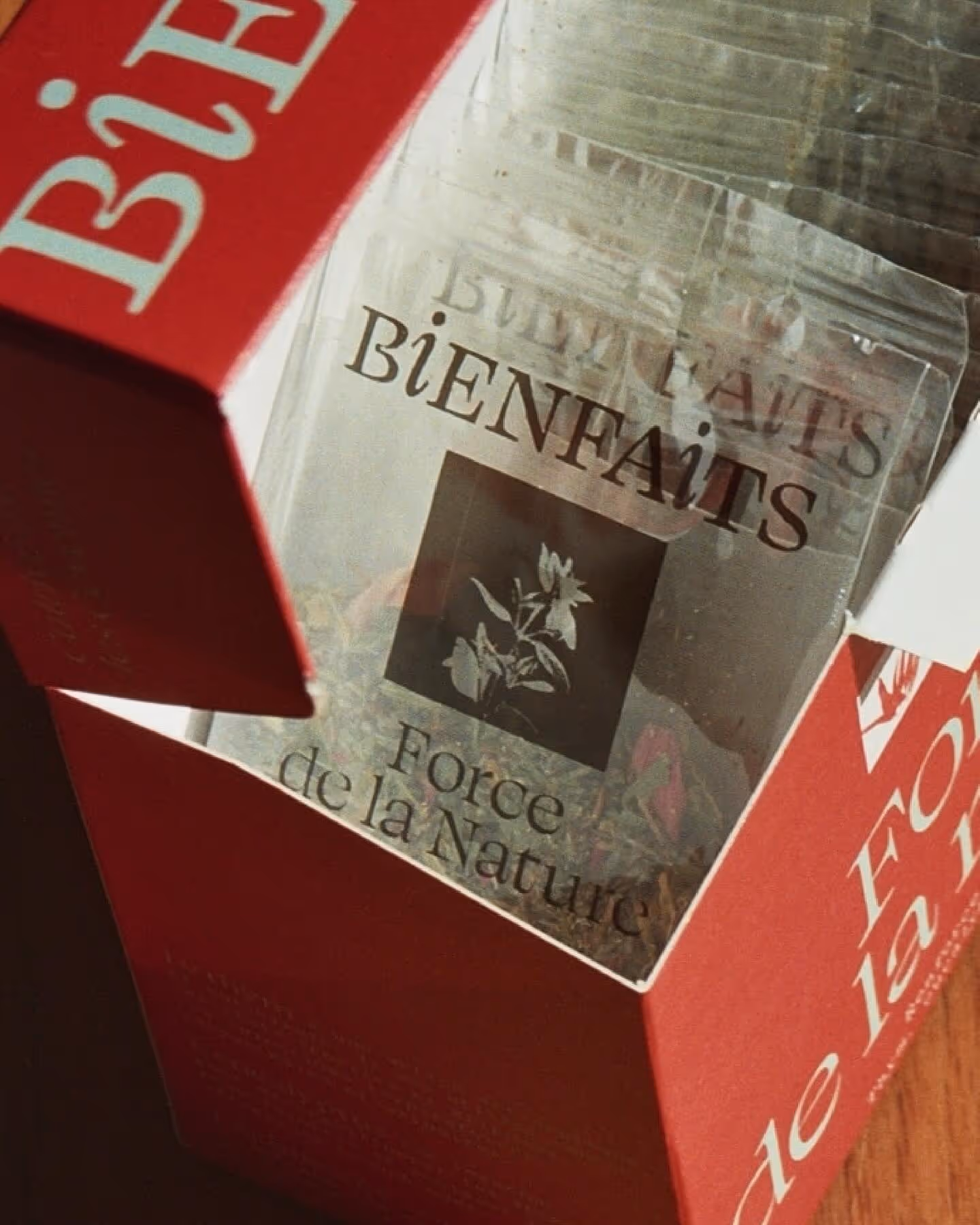 Boîte rouge ouverte contenant un sachet transparent marqué BIENFAITS Force de la Nature avec une illustration de fleurs.