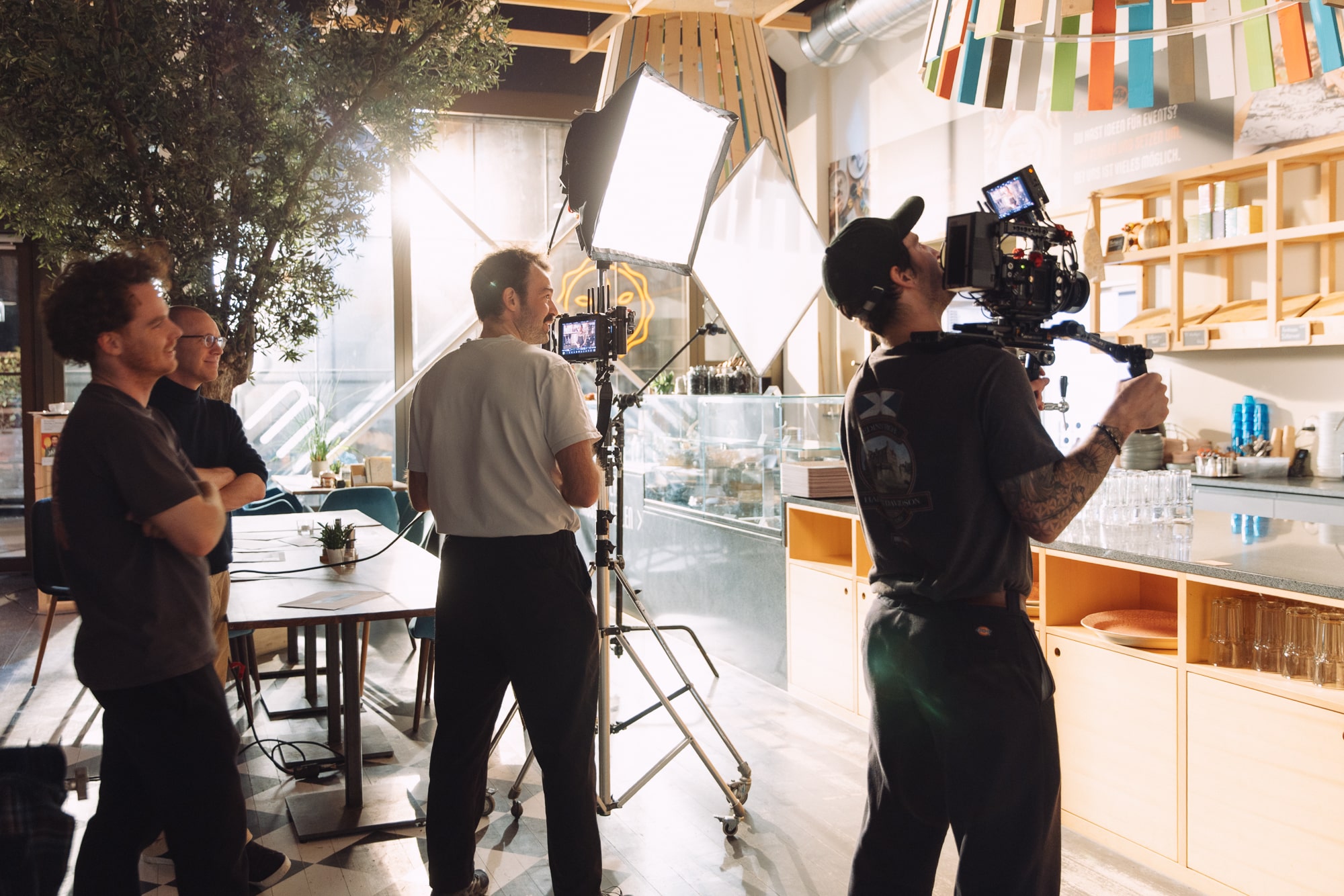 Film crew captures indoor footage in cozy cafe with expert lighting equipment and camera setup.