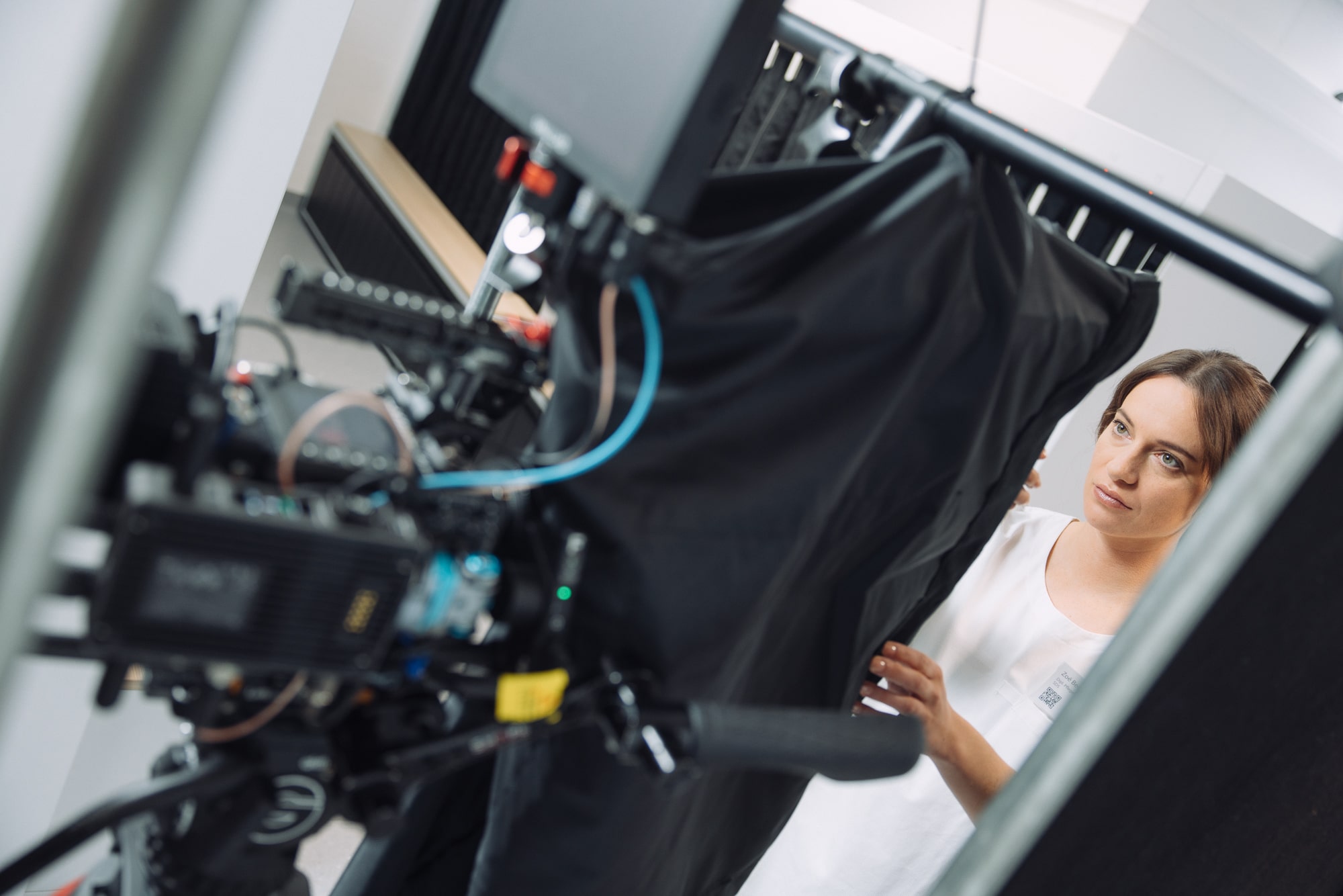 Woman in white dress adjusting fabric near professional camera equipment setup on location shoot.