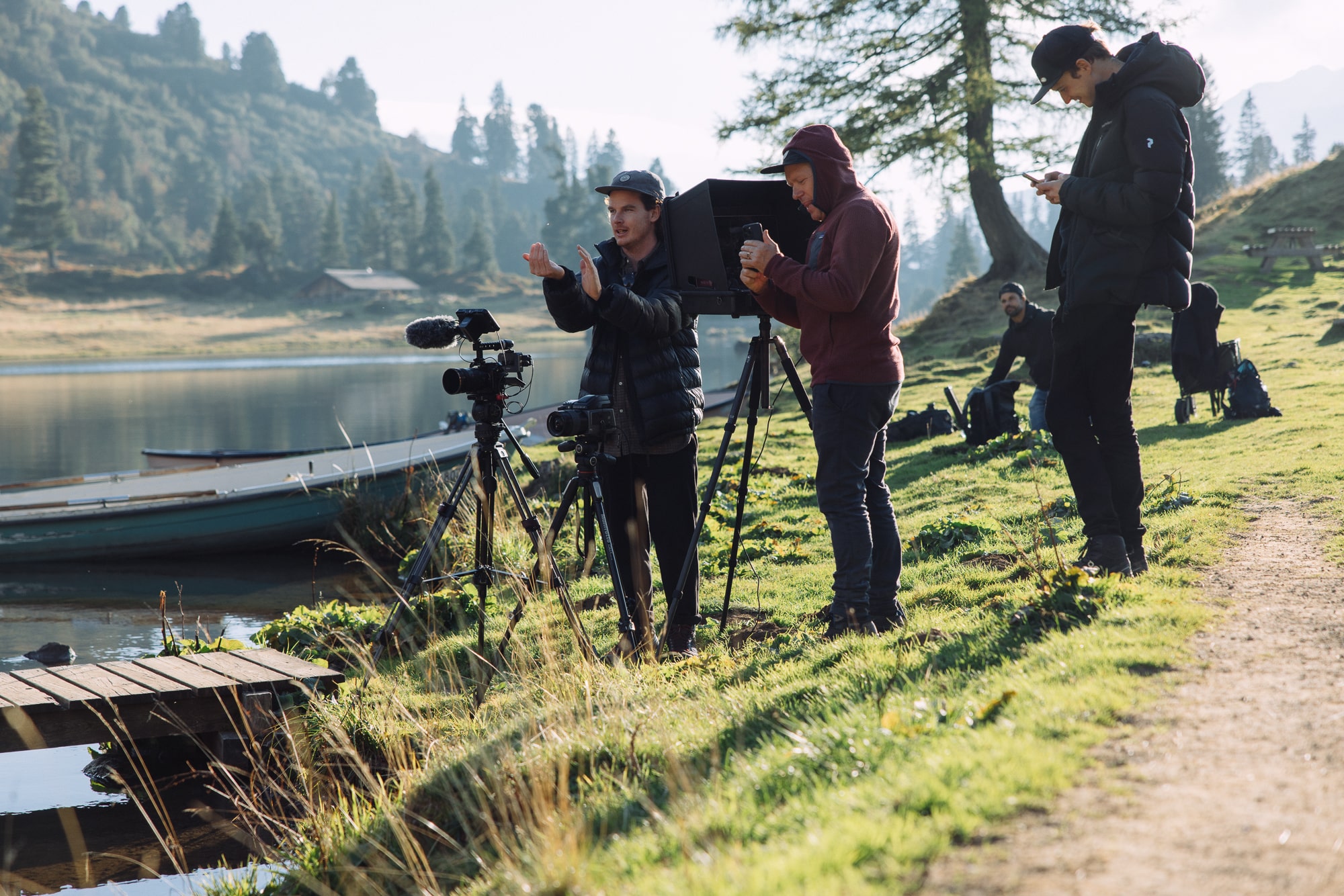 Professional film crew setting up equipment by serene lake with stunning mountain backdrop.