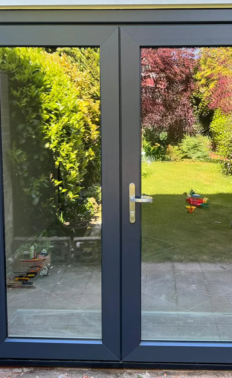 Donkergrijze kunststof tuindeuren met grote glaspartijen en metalen deurklink, uitkijkend op een groene tuin.