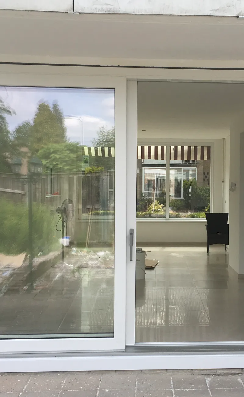 Witte kunststof schuifpui met grote glaspartijen die toegang geeft tot de tuin en veel licht in de woonkamer brengt.