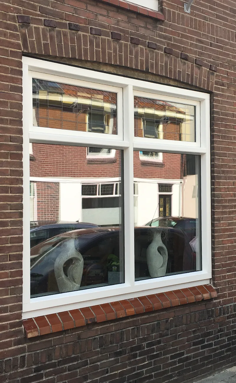 Woonkamerraam met wit kunststof kozijn en roodbruine vensterbanktegels in een klassieke bakstenen gevel.