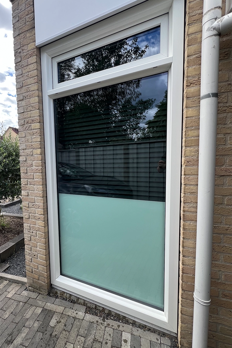 Voordeurraam met witte kozijnen en deels matglas aan de onderzijde in een bakstenen gevel.