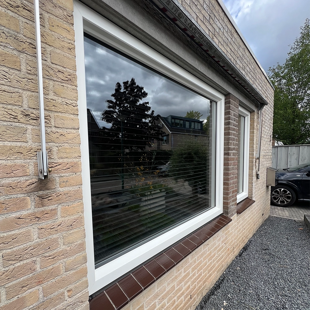 Groot woonkamerraam met witte kunststof kozijnen en vensterbank in een bakstenen gevel.