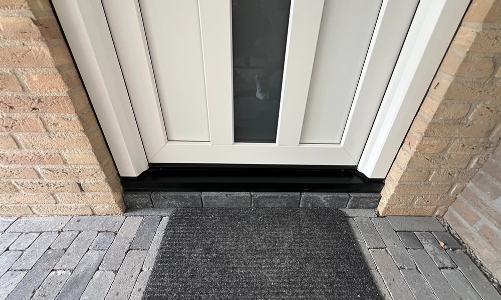Voordeur met witte kunststof panelen, glazen inzetstuk en zwarte dorpel op een bakstenen gevel.