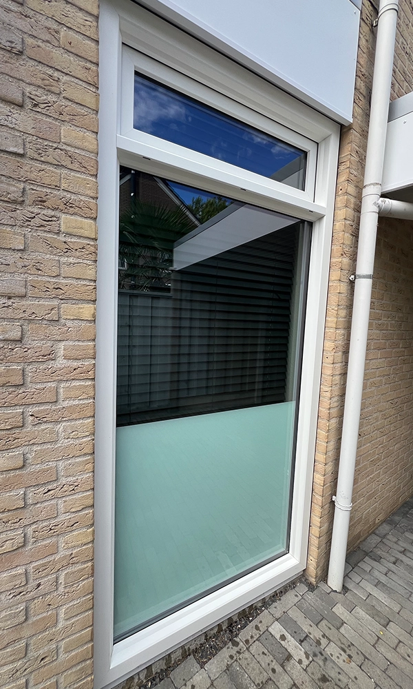 Raam met wit kunststof kozijn en deels matglas aan de onderzijde in een bakstenen gevel.