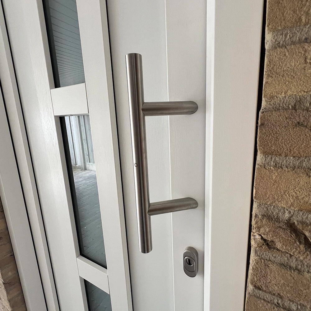 Witte voordeur met verticale glazen inzetstukken, roestvrijstalen deurhendel en slot in een bakstenen gevel.