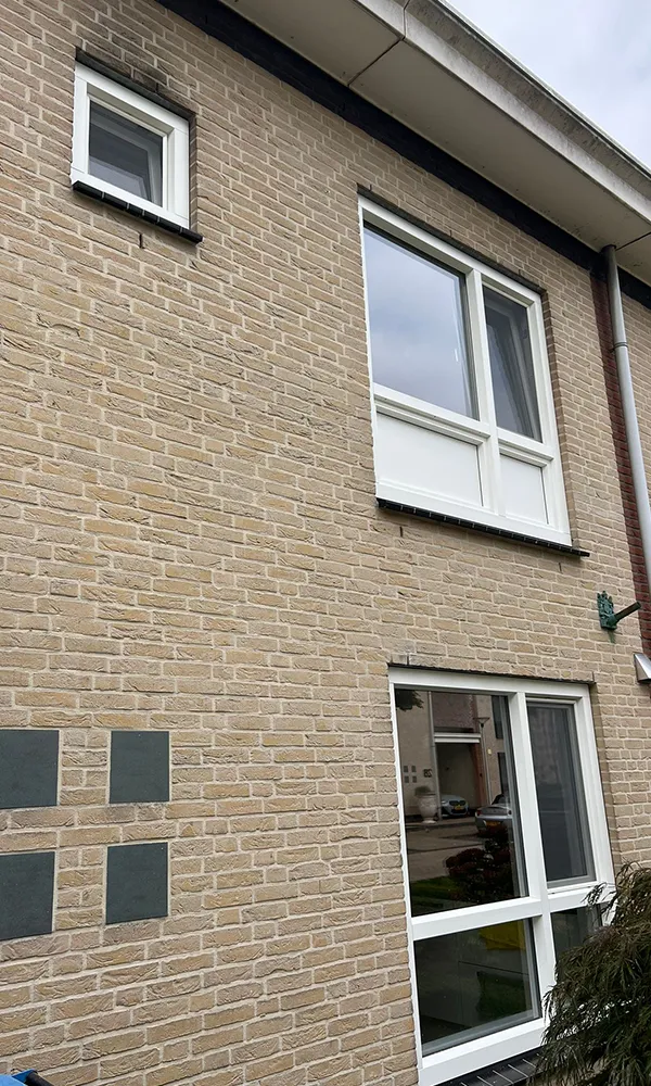Voorgevel van een woning met kunststof kozijnen, bestaande uit een klein bovenraam, een groter raam op de verdieping en een raam met deur op de begane grond.
