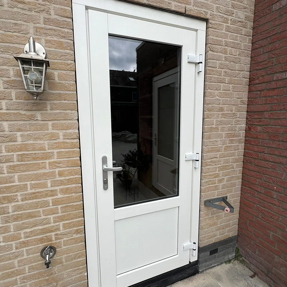 Witte kunststof achterdeur met groot glasvlak in een gemetselde gevel, naast buitenlamp en waterkraan.