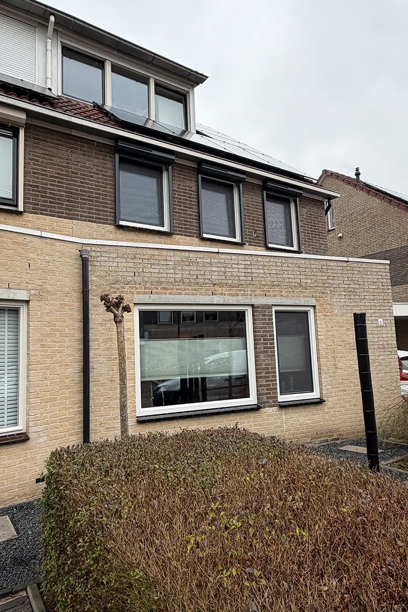 Woning met witte kunststof kozijnen en zwarte rolluiken in bakstenen gevel, voorzien van onderhoudsarme en energiezuinige afwerking.