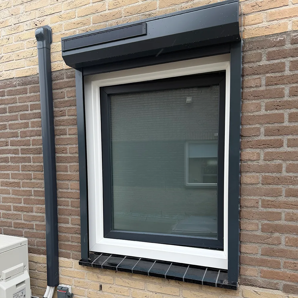 Wit kunststof kozijn met antraciet rolluik in bakstenen gevel, onderhoudsarm en strak afgewerkt.