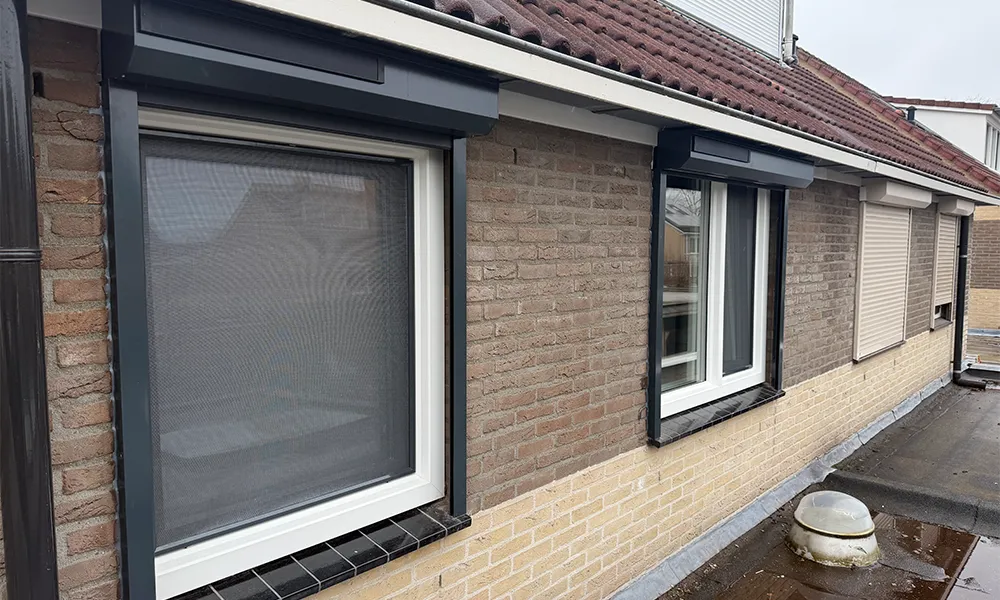 Witte kunststof kozijnen met antraciet rolluiken in bakstenen gevel, onderhoudsarm en energiezuinig geplaatst.