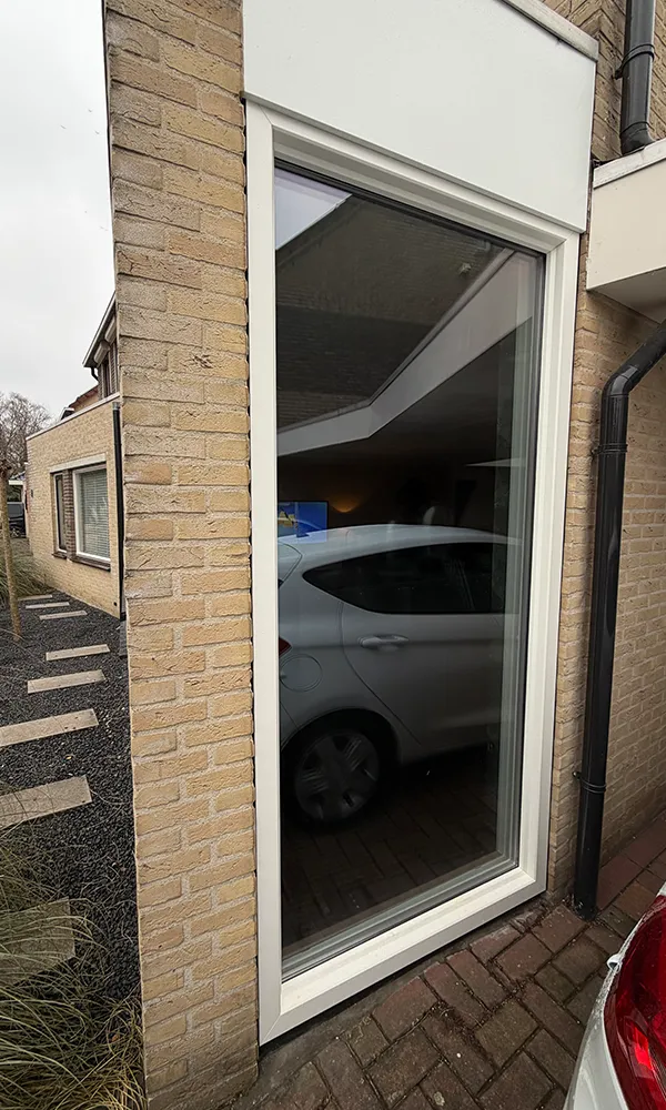 Hoog wit kunststof kozijn met vaste beglazing in bakstenen gevel, strak geplaatst en onderhoudsarm uitgevoerd.