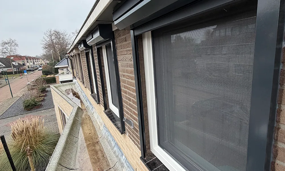 Witte kunststof kozijnen met antraciet rolluiken op bovenverdieping, strak geplaatst in bakstenen gevel en onderhoudsarm uitgevoerd.