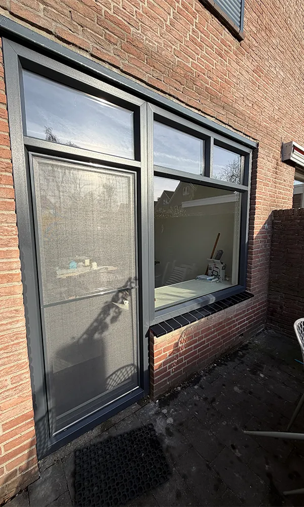 Antraciet kunststof kozijn en deur met bovenlichten in bakstenen gevel, strak geplaatst en voorzien van onderhoudsarme afwerking.