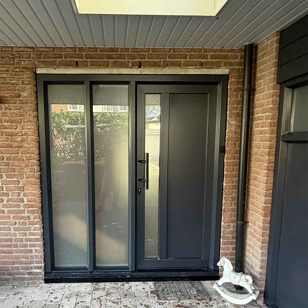 Antraciet kunststof achterdeur met zijlichten onder overkapping, strak geplaatst in bakstenen gevel en onderhoudsarm uitgevoerd.