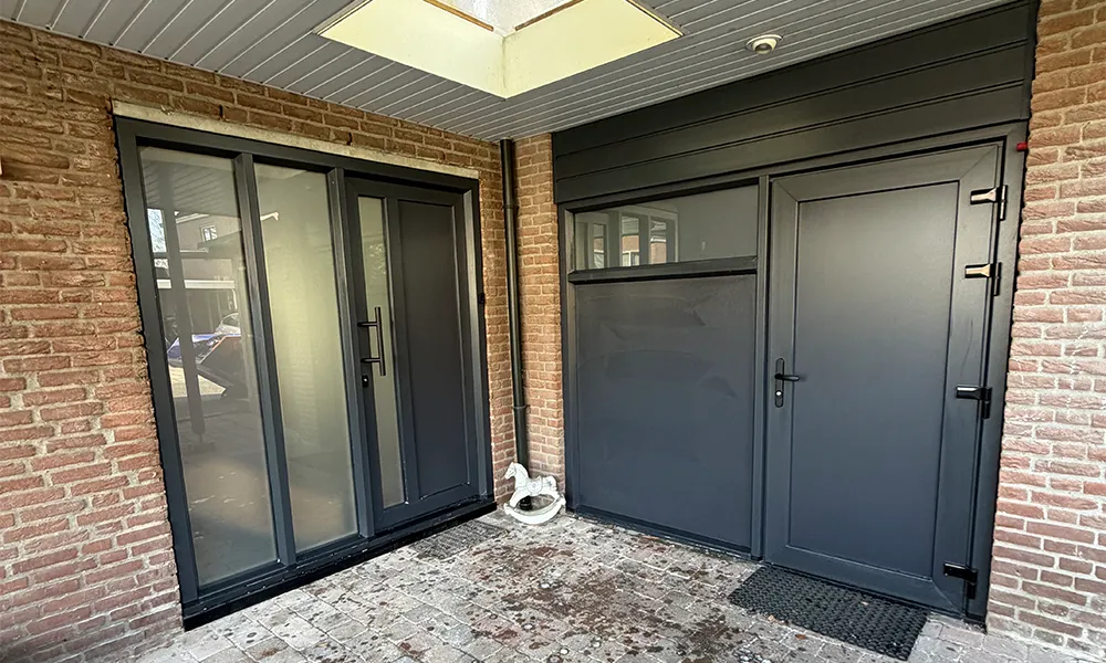 Antraciet kunststof achterdeur en kozijnen onder overkapping, strak geplaatst in bakstenen gevel met onderhoudsarme afwerking.