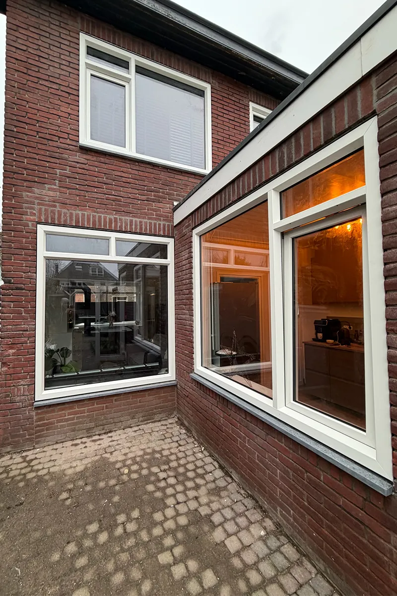 Witte kunststof kozijnen in bakstenen gevel met vaste raampartijen en bovenlichten, strak geplaatst en energiezuinig uitgevoerd.