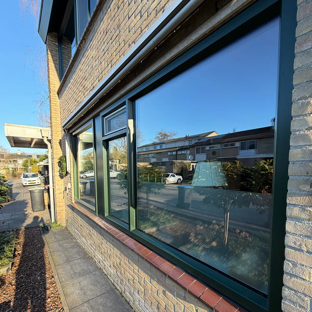 Groene kunststof kozijnen in bakstenen gevel met grote raampartij en strakke afwerking, onderhoudsarm en energiezuinig uitgevoerd.