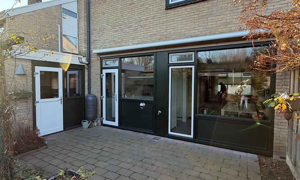 Achtergevel met donkergroene kunststof kozijnen en deuren, voorzien van grote glaspartijen en onderhoudsarme afwerking in bakstenen woning.