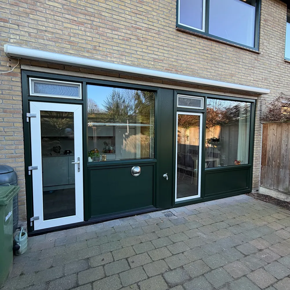 Achtergevel met donkergroene kunststof kozijnen en deuren, grote glaspartijen en strakke, onderhoudsarme afwerking in bakstenen woning.