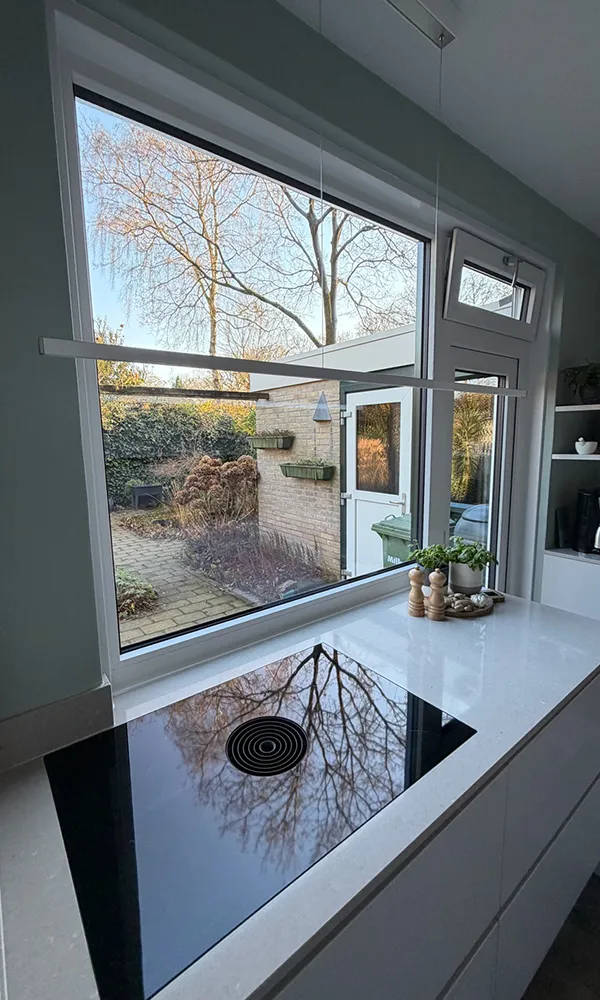Binnenaanzicht van groot kunststof kozijn met vaste raampartij en bovenlicht, geplaatst in moderne keuken met uitzicht op tuin.