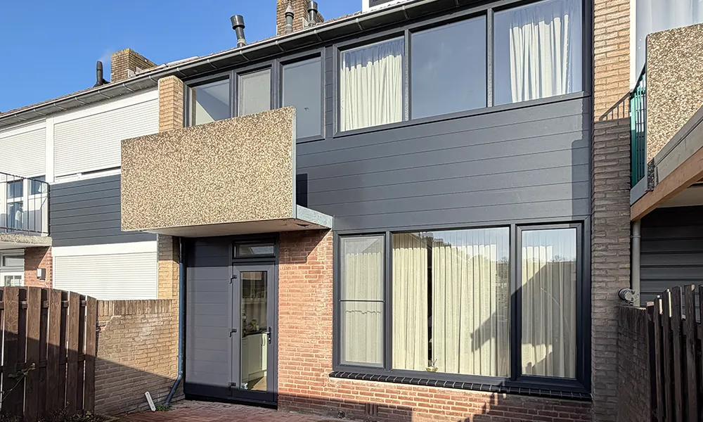Tussenwoning met antraciet kunststof kozijnen, moderne voordeur en strakke gevelbekleding gecombineerd met bakstenen gevel en balkon.