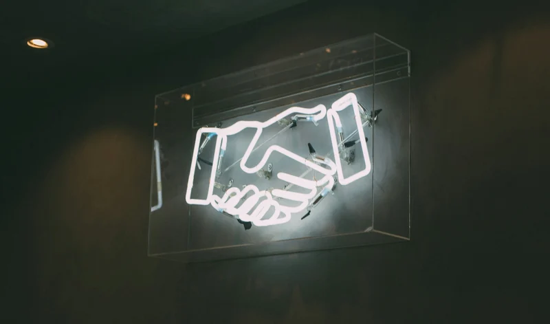 Neon sign of a handshake symbol on a dark wall.