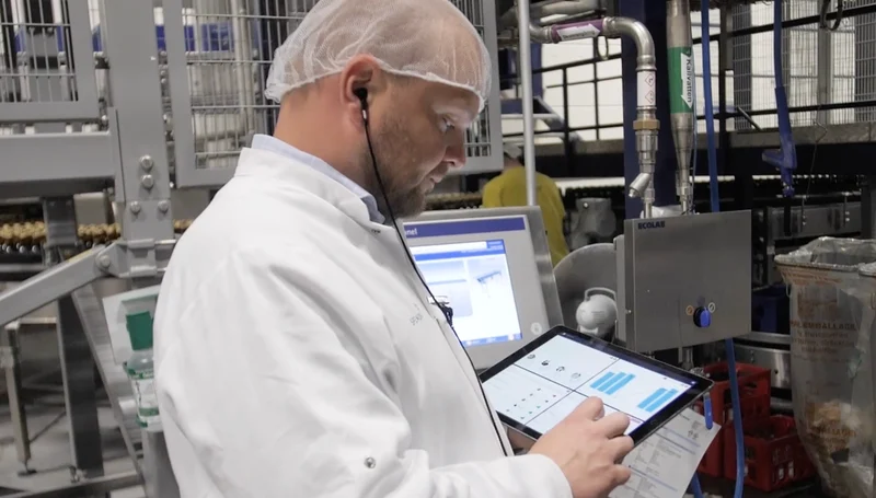 Factory worker in protective clothing using a tablet on the production floor.