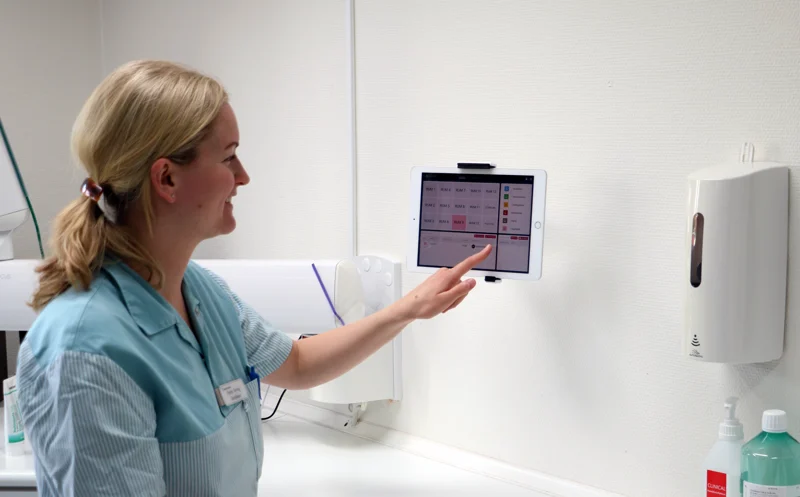 Healthcare professional using a mounted tablet displaying a digital board.
