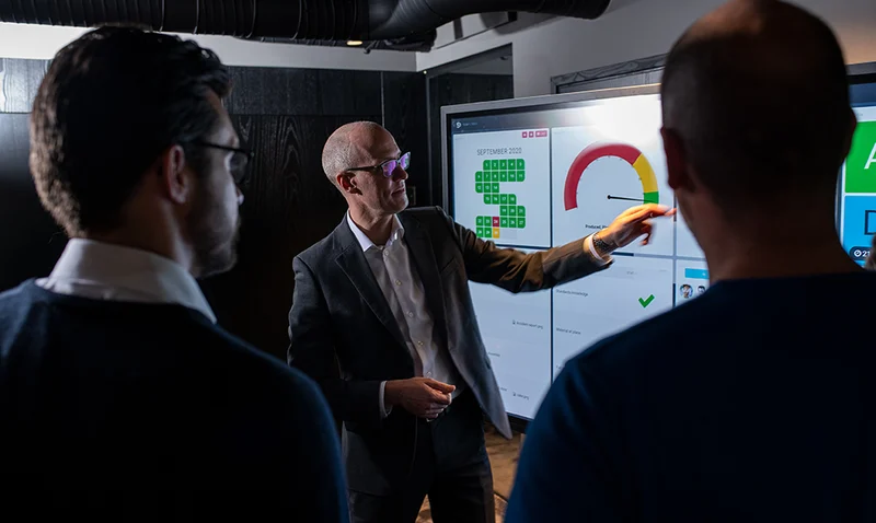Business professional presenting a digital dashboard with a performance gauge on a large screen to colleagues.