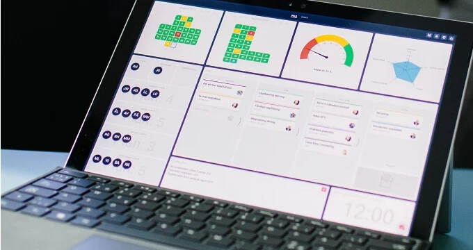 Laptop showing a digital dashboard with status indicators, gauges, and task boards.