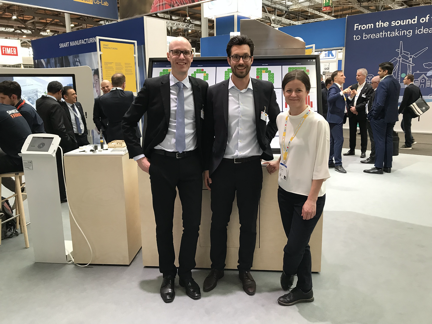 Three professionals standing in front of a digital board at a trade show booth.