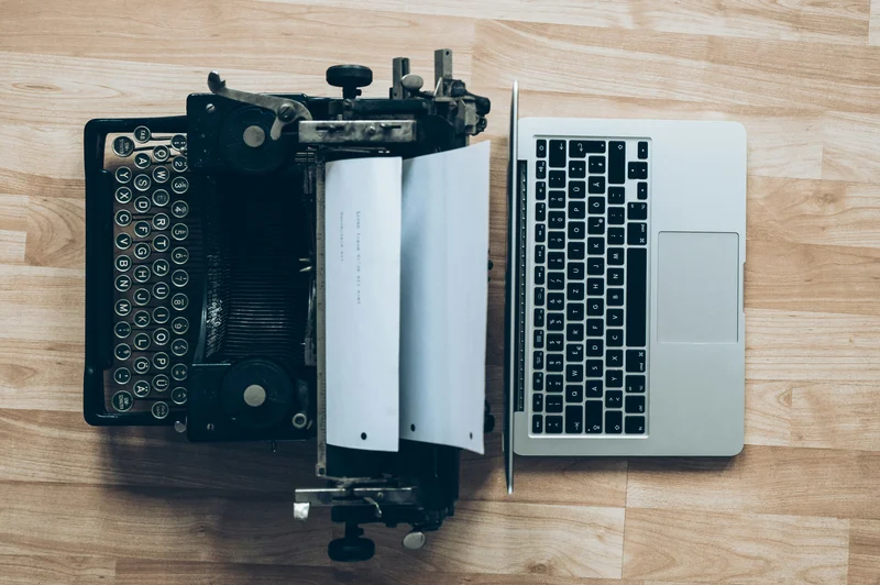 Vintage typewriter next to a modern laptop on a wooden desk.