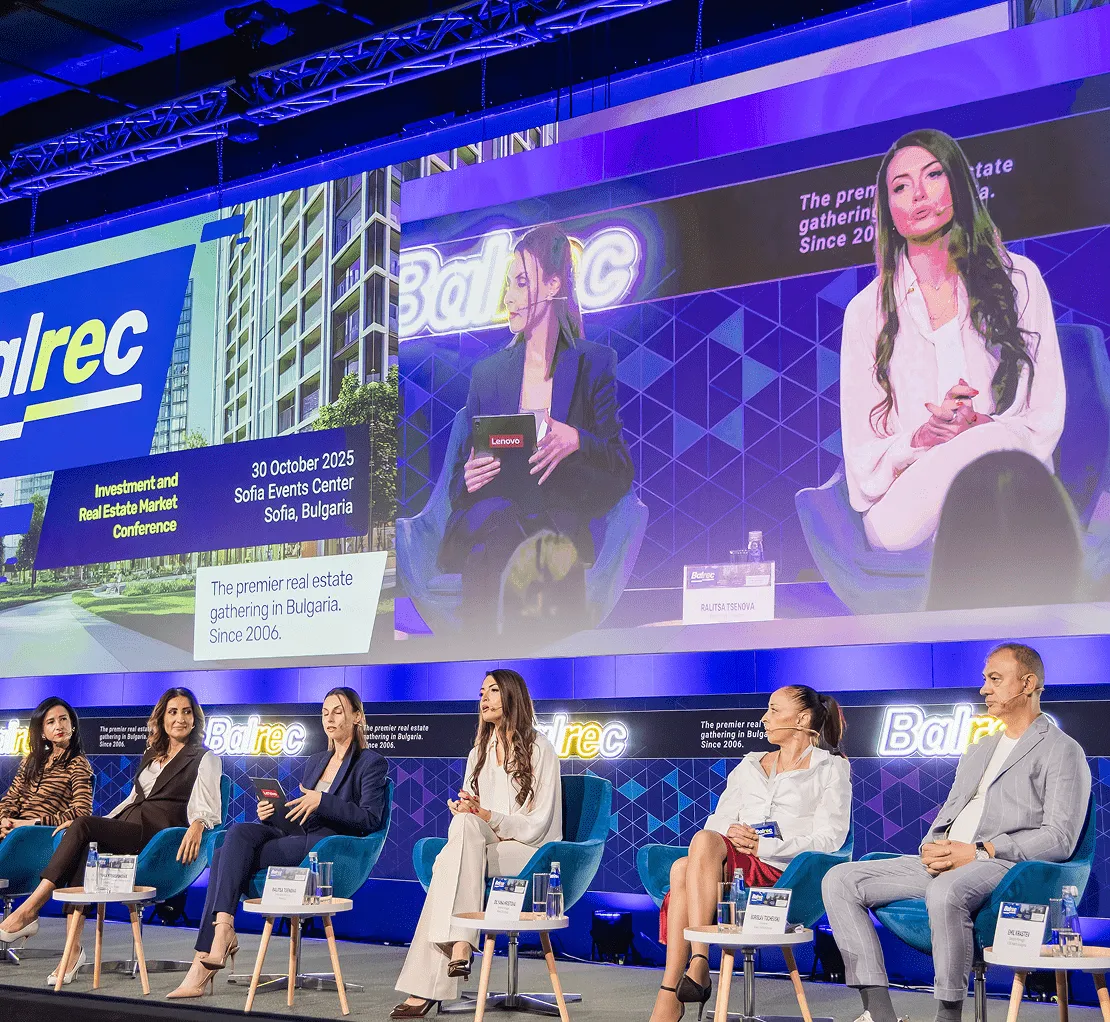 Панел от петима лектори, седнали на сцената със сини столове на конференцията за инвестиции и пазар на недвижими имоти Balrec на 30 октомври 2025 г., София, България, с голям екран, на който са изобразени две жени, говорещи заедно.