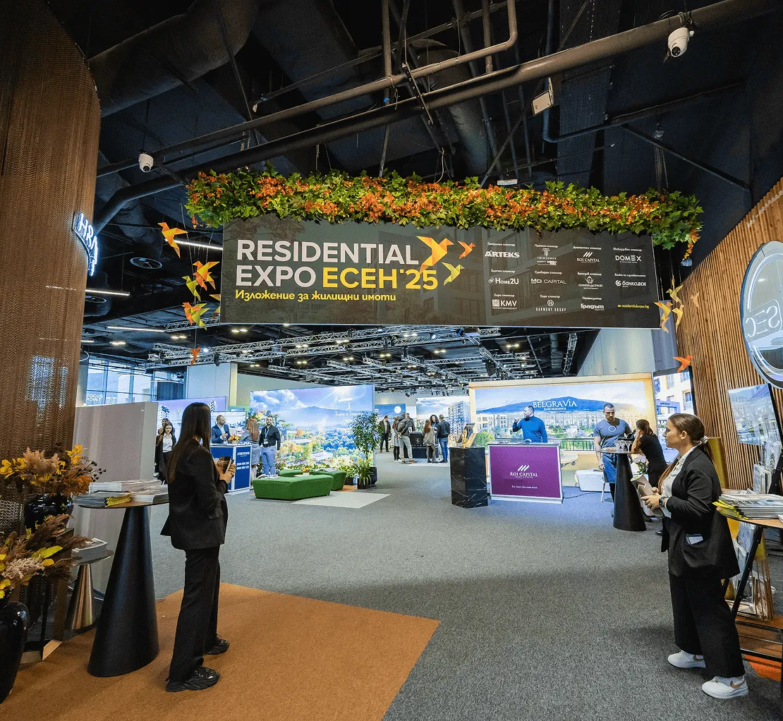 Закрито жилищно изложение с посетители и щандове, представящи жилищни проекти, под голям надпис „Residential Expo Ecen '25“ с декоративна зеленина отгоре.